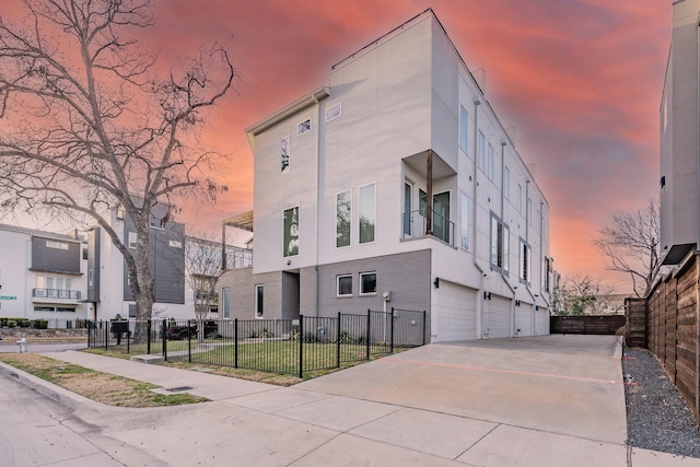 property at dusk with concrete driveway, fence, and a garage