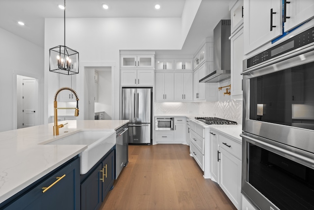 kitchen with blue cabinets, white cabinets, stainless steel appliances, wall chimney exhaust hood, and a sink