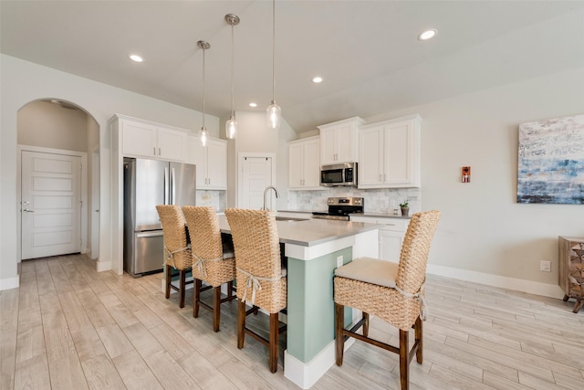 kitchen with a sink, arched walkways, appliances with stainless steel finishes, a breakfast bar area, and decorative backsplash