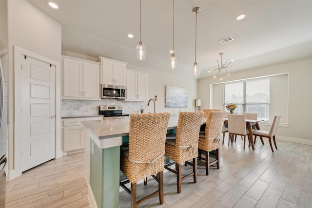 kitchen with visible vents, a breakfast bar, an island with sink, decorative backsplash, and appliances with stainless steel finishes