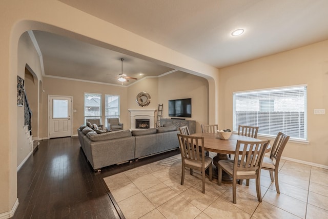 dining space featuring ceiling fan, baseboards, ornamental molding, a fireplace, and light wood-style floors