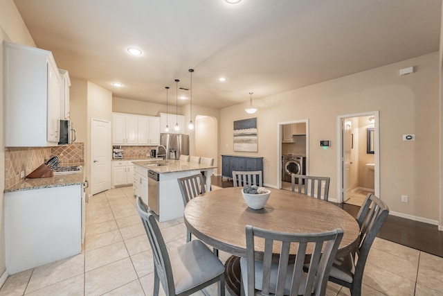 dining space featuring baseboards, light tile patterned floors, recessed lighting, arched walkways, and washer / clothes dryer