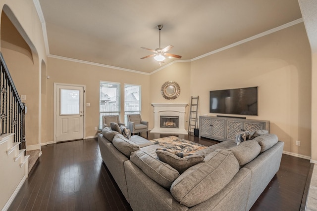 living area with a fireplace with raised hearth, dark wood finished floors, stairway, crown molding, and baseboards