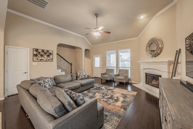 living room featuring visible vents, dark wood-style floors, a glass covered fireplace, arched walkways, and crown molding