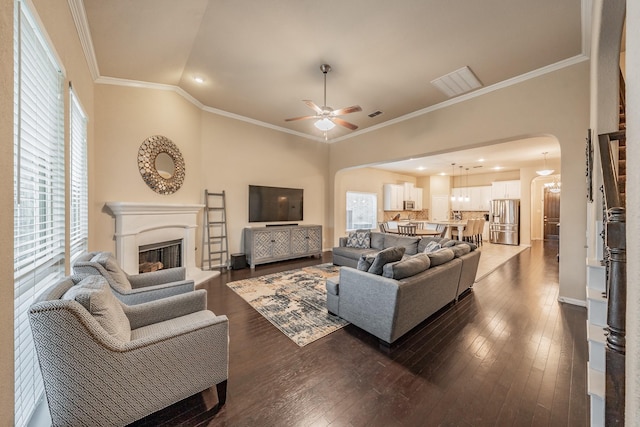 living area featuring ornamental molding, a ceiling fan, arched walkways, a fireplace, and dark wood-style flooring