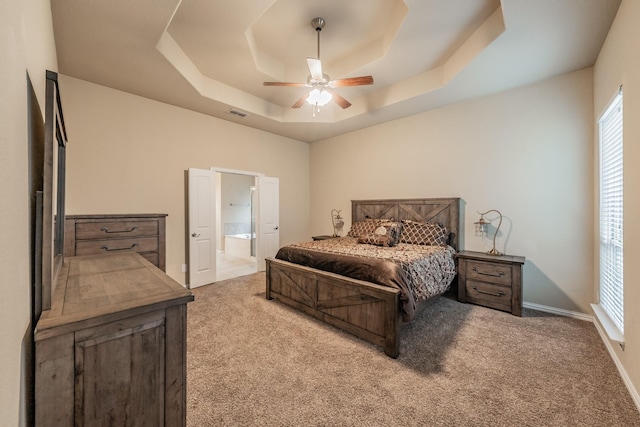 carpeted bedroom with visible vents, baseboards, ceiling fan, ensuite bath, and a raised ceiling