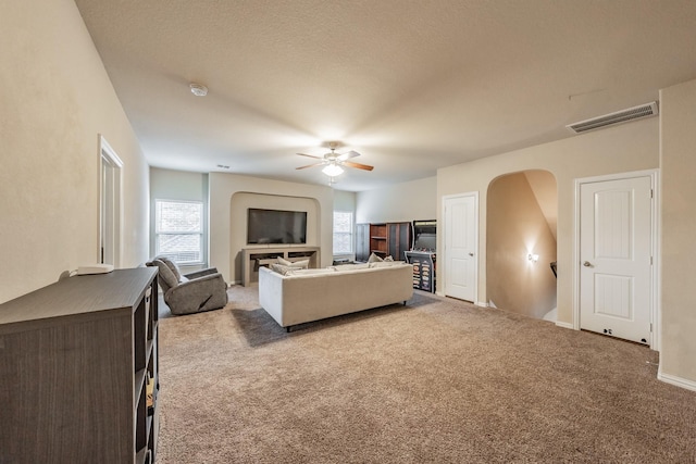 carpeted living area with arched walkways, visible vents, and ceiling fan