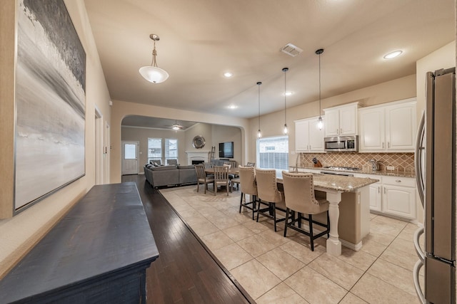 kitchen with visible vents, arched walkways, decorative backsplash, appliances with stainless steel finishes, and open floor plan