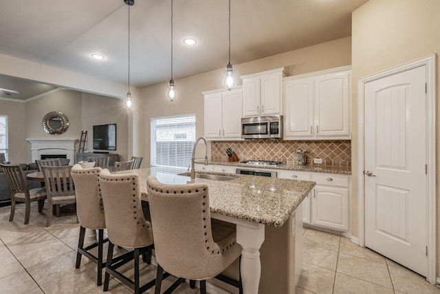 kitchen featuring light stone counters, a center island with sink, a sink, stainless steel microwave, and backsplash