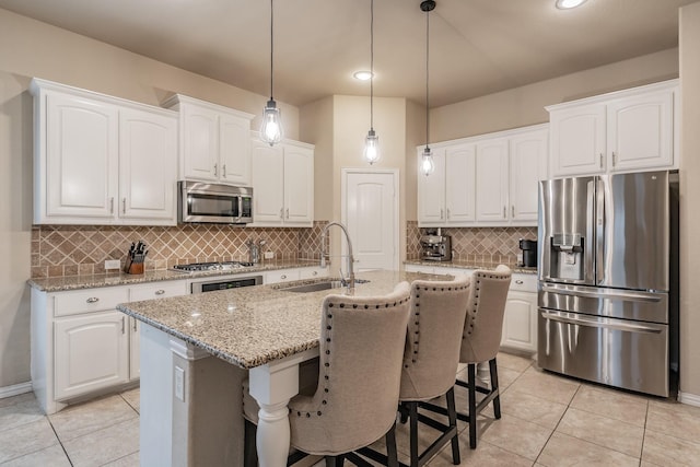 kitchen featuring a kitchen island with sink, a sink, white cabinetry, stainless steel appliances, and light stone countertops