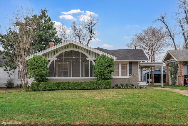 view of front of home featuring an attached carport, a front yard, a sunroom, brick siding, and a chimney