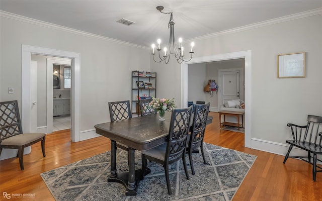 dining space with a notable chandelier, wood finished floors, visible vents, and ornamental molding