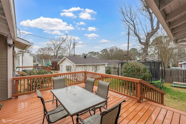 wooden terrace with outdoor dining space, a trampoline, and fence