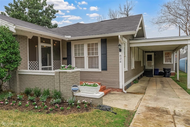 view of front of property with roof with shingles, a sunroom, entry steps, concrete driveway, and a carport