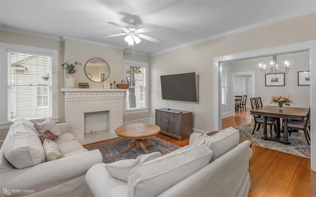 living area featuring a brick fireplace, crown molding, ceiling fan, baseboards, and wood finished floors