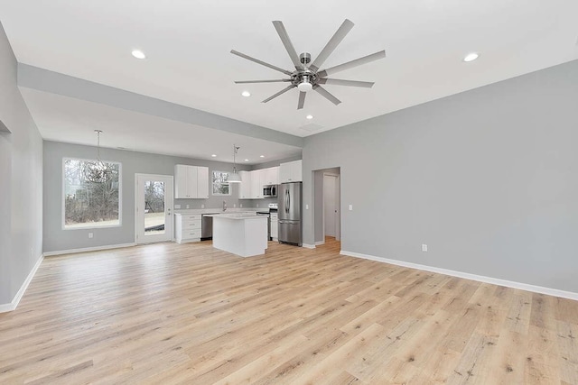 kitchen featuring open floor plan, a center island, stainless steel appliances, light wood-style floors, and white cabinets