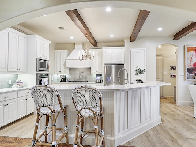 kitchen featuring visible vents, light wood-style flooring, arched walkways, custom range hood, and appliances with stainless steel finishes