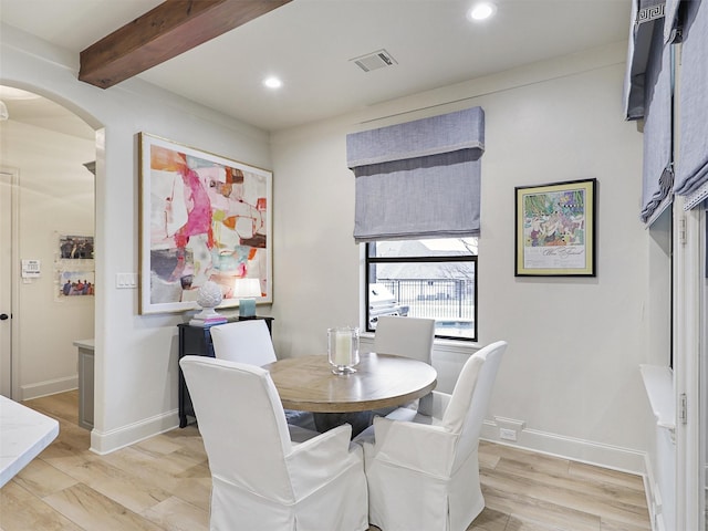 dining room with beam ceiling, visible vents, arched walkways, and light wood finished floors