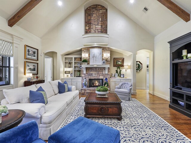 living room with wood finished floors, visible vents, a fireplace, arched walkways, and beamed ceiling