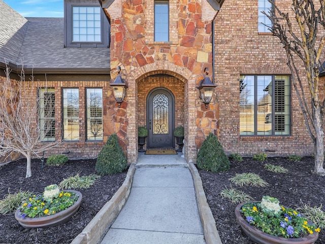 doorway to property with brick siding and a shingled roof