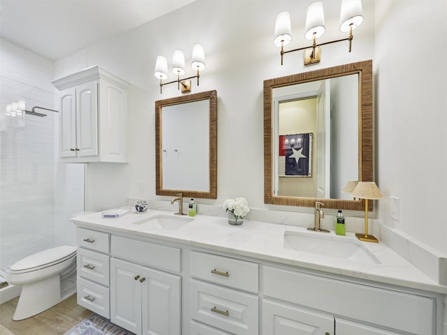 bathroom with a sink, toilet, double vanity, and a tile shower