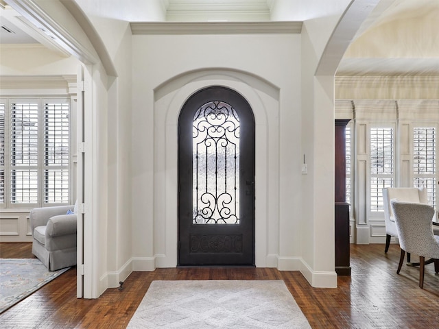 entrance foyer featuring baseboards, arched walkways, dark wood-style flooring, and ornamental molding