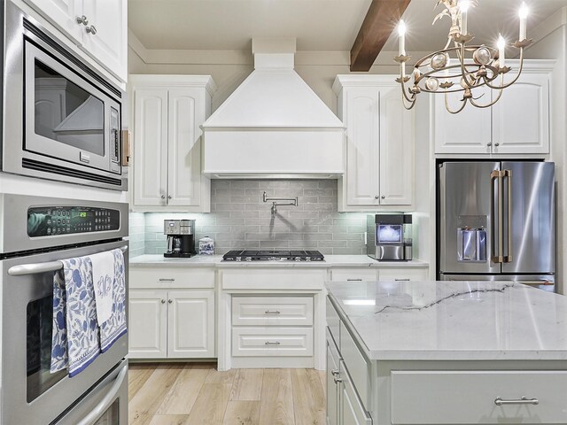 kitchen with decorative backsplash, custom range hood, white cabinetry, and stainless steel appliances