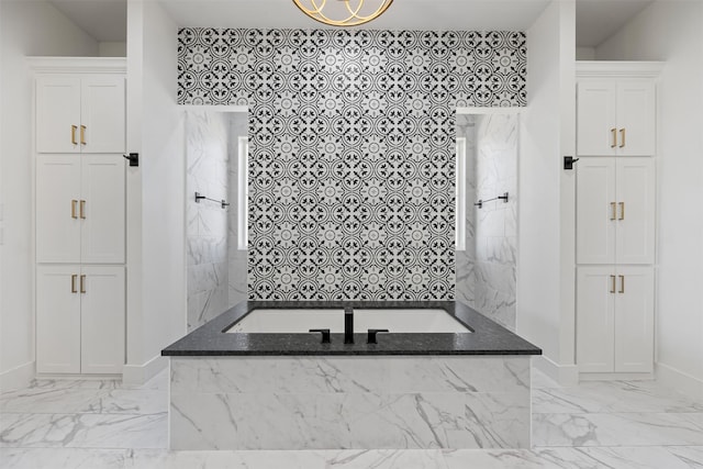 bathroom featuring a relaxing tiled tub, baseboards, and marble finish floor