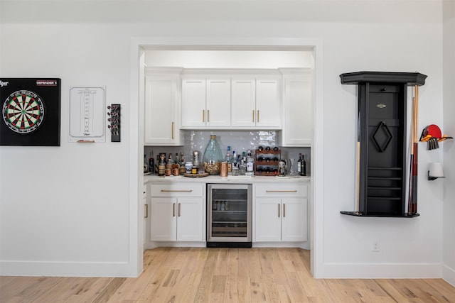 bar with wine cooler, baseboards, bar, tasteful backsplash, and light wood finished floors