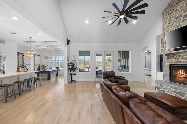 living room featuring visible vents, a stone fireplace, light wood-style flooring, french doors, and arched walkways