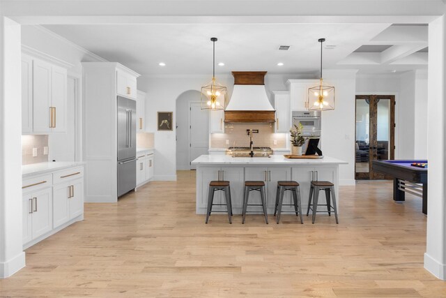 kitchen featuring white cabinets, appliances with stainless steel finishes, a breakfast bar area, premium range hood, and tasteful backsplash