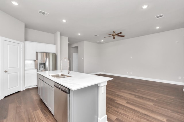 kitchen with a sink, dark wood-type flooring, appliances with stainless steel finishes, and a center island with sink