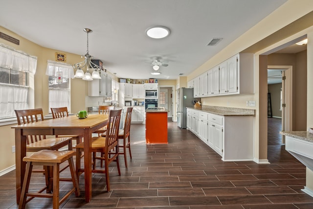 kitchen with wood finish floors, visible vents, ceiling fan with notable chandelier, stainless steel appliances, and white cabinets