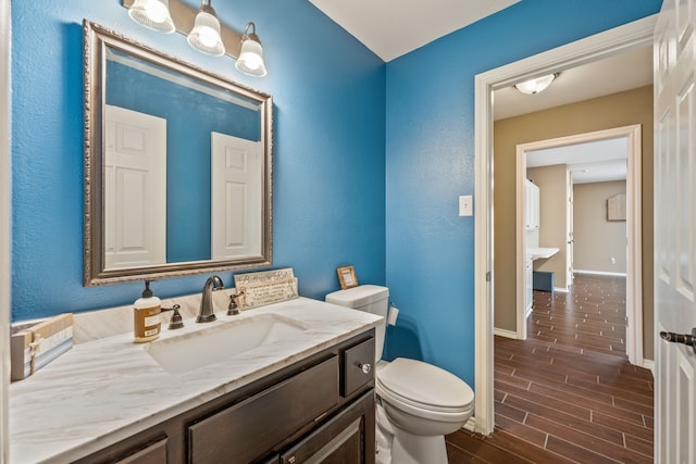 half bathroom with vanity, toilet, baseboards, and wood tiled floor