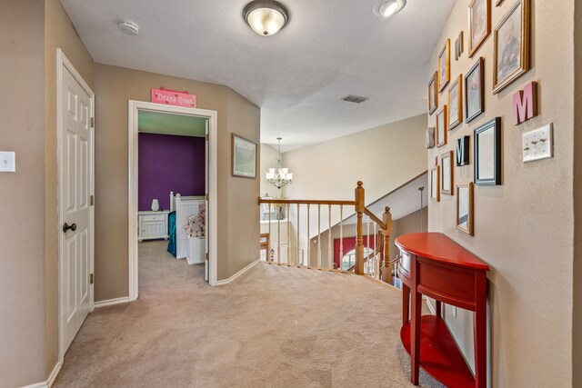 corridor with visible vents, an upstairs landing, a notable chandelier, carpet floors, and baseboards