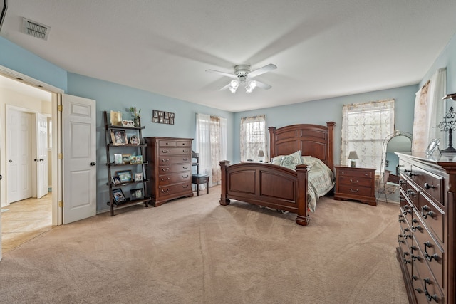 bedroom with light carpet, visible vents, and a ceiling fan