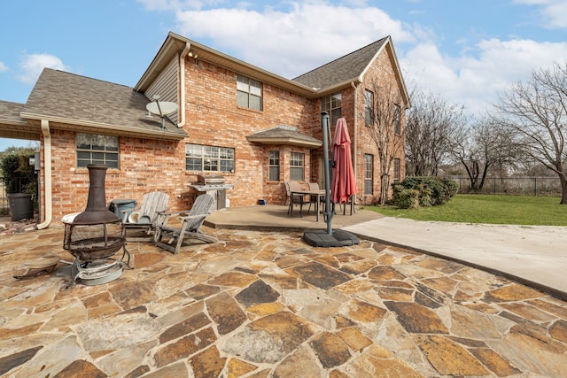 back of property with brick siding, a shingled roof, fence, an outdoor fire pit, and a patio