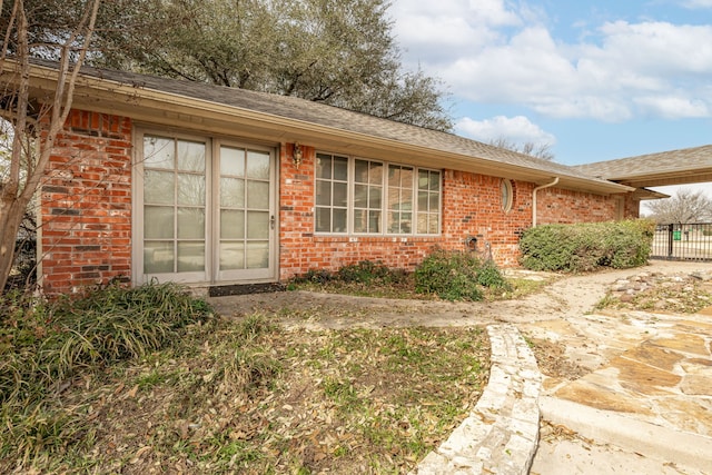 doorway to property featuring fence, brick siding, and a shingled roof