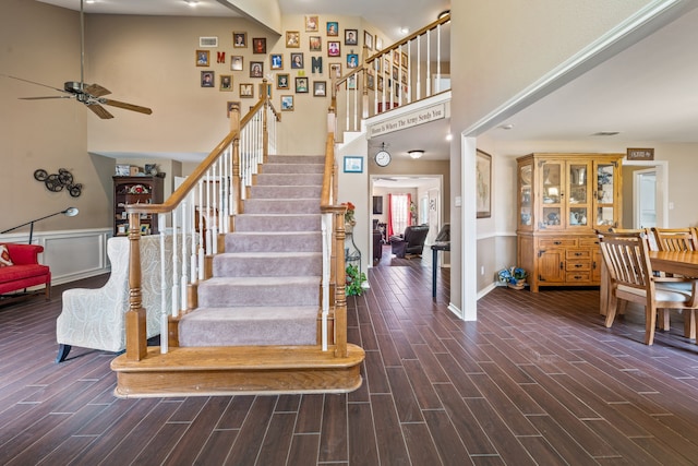 stairs with ceiling fan, baseboards, wood finish floors, and a towering ceiling