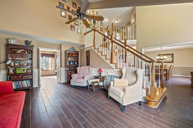 living area with stairway, ceiling fan with notable chandelier, a towering ceiling, and wood tiled floor