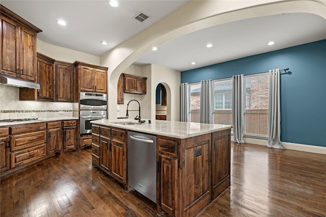 kitchen with under cabinet range hood, appliances with stainless steel finishes, arched walkways, dark wood-style floors, and a sink