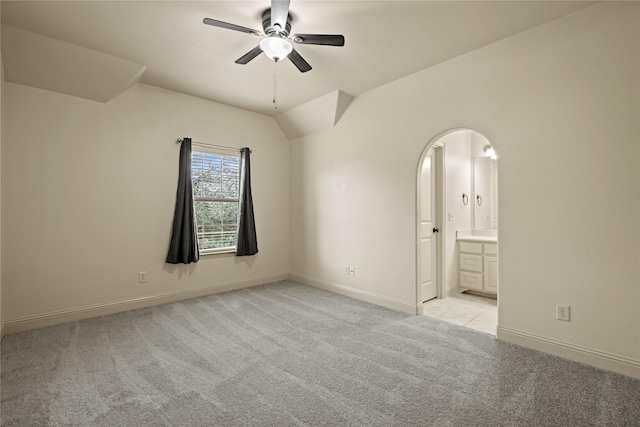 unfurnished room with baseboards, vaulted ceiling, light carpet, arched walkways, and a ceiling fan