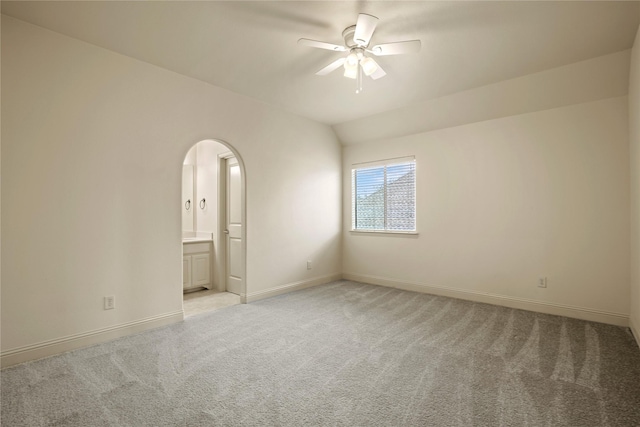 spare room with baseboards, lofted ceiling, arched walkways, ceiling fan, and light carpet