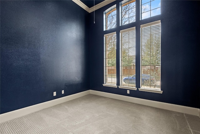 carpeted spare room with baseboards, a wealth of natural light, and ornamental molding