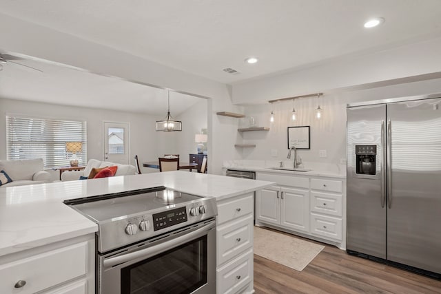 kitchen featuring open floor plan, appliances with stainless steel finishes, wood finished floors, white cabinetry, and a sink