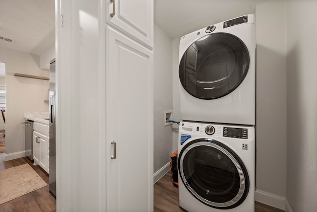 laundry area with dark wood-type flooring, stacked washer / dryer, visible vents, and baseboards