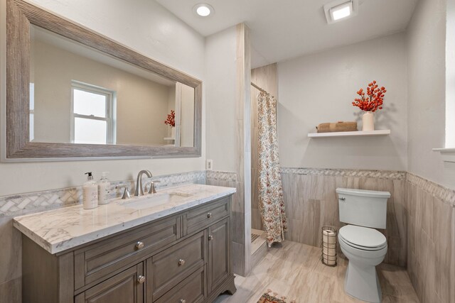 bathroom with a wainscoted wall, toilet, tile walls, and vanity