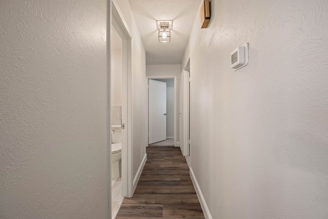 hall with baseboards, wood finished floors, and a textured wall