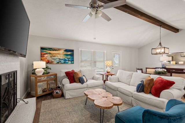 living room featuring ceiling fan with notable chandelier, a fireplace, vaulted ceiling with beams, and wood finished floors