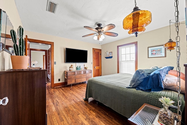 bedroom with ceiling fan, visible vents, baseboards, and wood finished floors